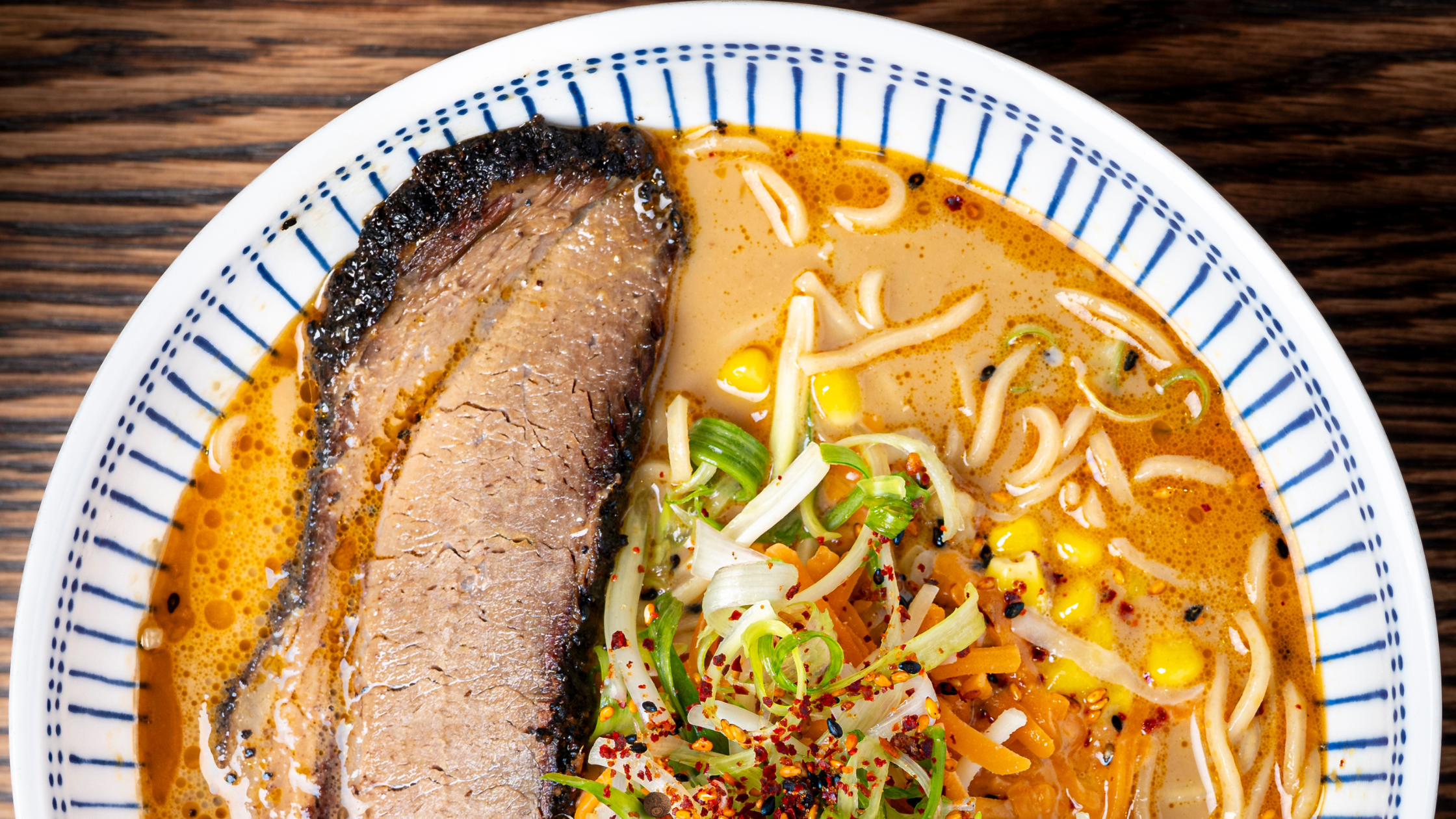 Topdown view of a bowl of Pitmaster's Brisket Ramen with broth, smoked brisket, noodles, and toppings.