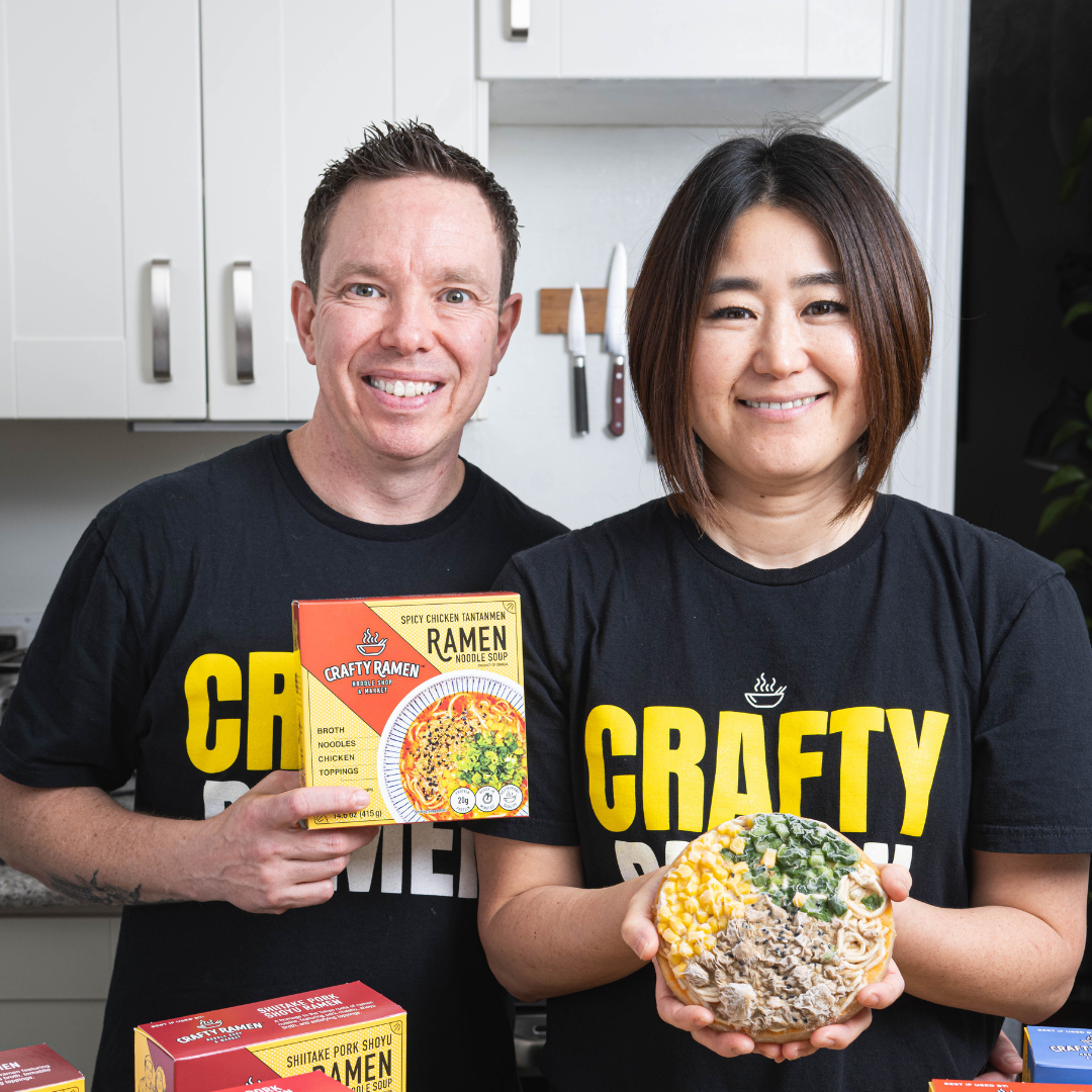Jared and Miki holding boxes and pucks of frozen ramen while wearing Crafty Ramen t-shirts