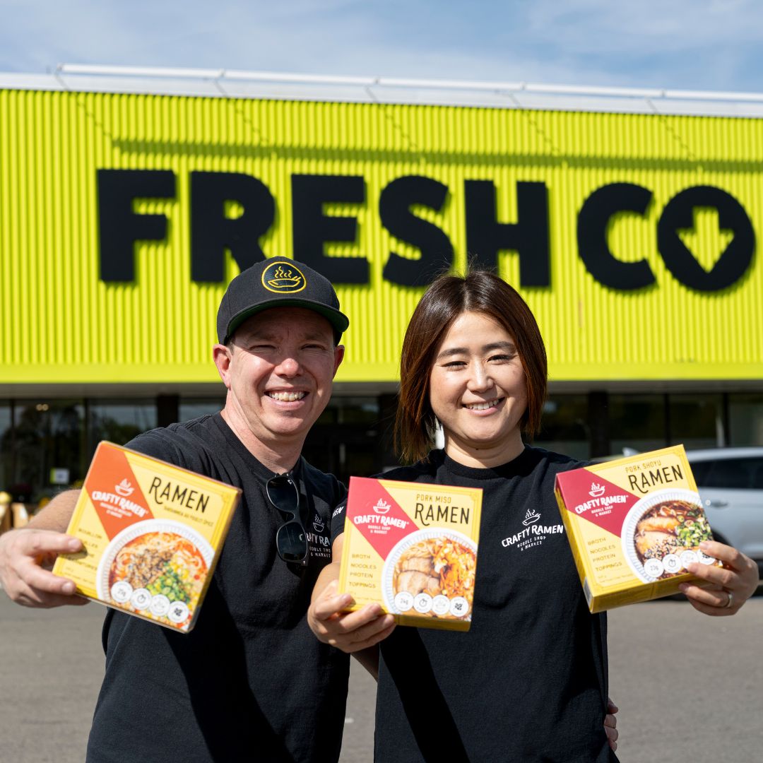 Jared and Miki standing outside of FreshCo holding boxes of Spicy Chicken Tantanmen Frozen Ramen, Pork Miso Frozen Ramen and Pork Shoyu Frozen Ramen