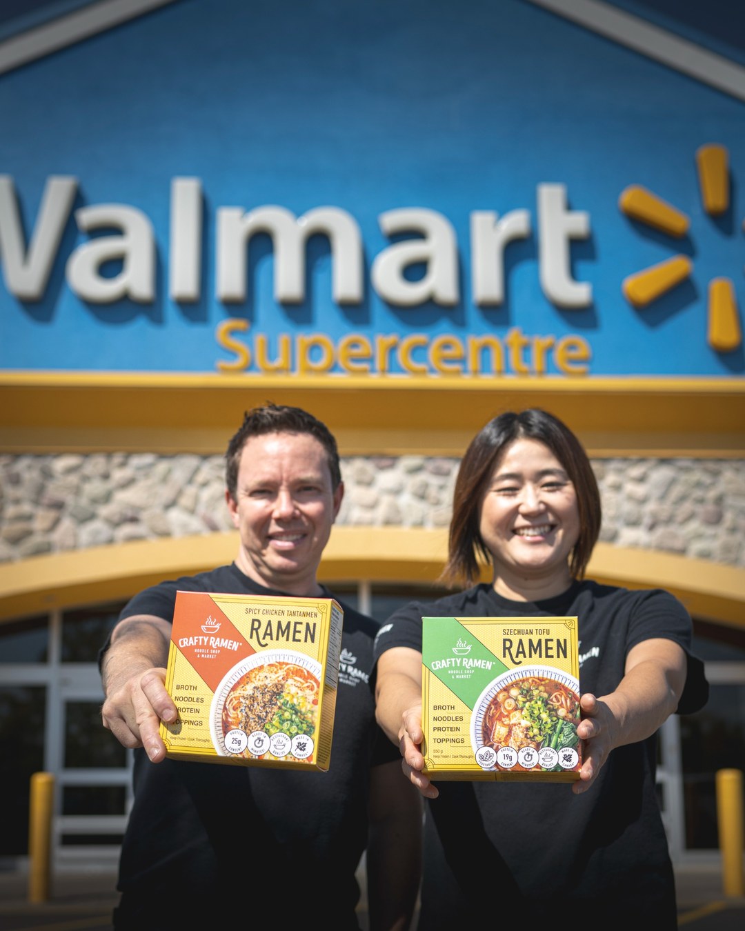 Jared and Miki standing outside of Walmart holding boxes of Spicy Chicken Tantanmen Frozen Ramen and Szechuan Tofu Frozen Ramen while wearing Crafty Ramen t-shirts.