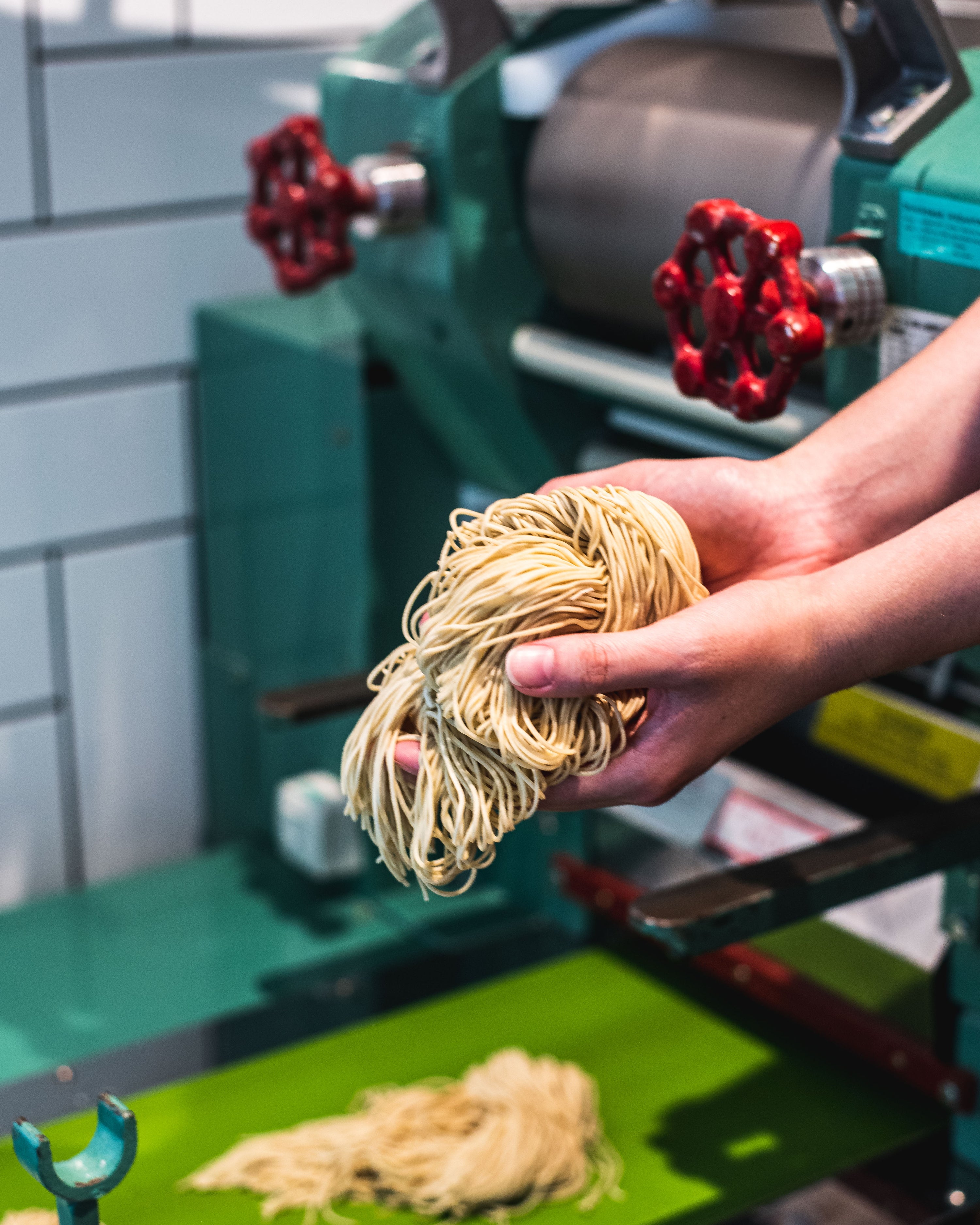 Two hands holding scratch-made ramen noodles in front of a noodle pulling machine