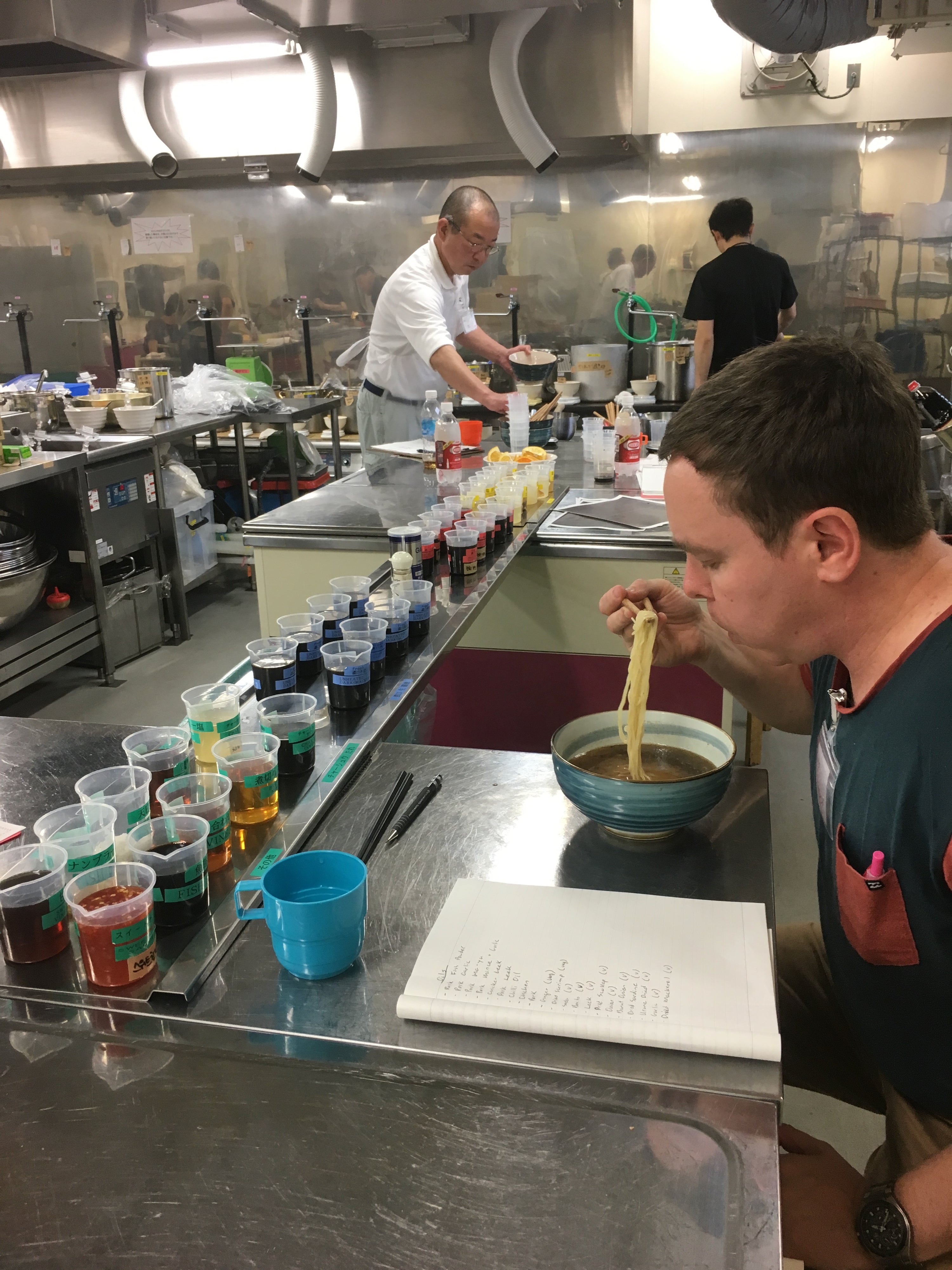Jared eating a bowl of ramen at a counter with various condiments in a kitchen setting at the Yamato School of Ramen
